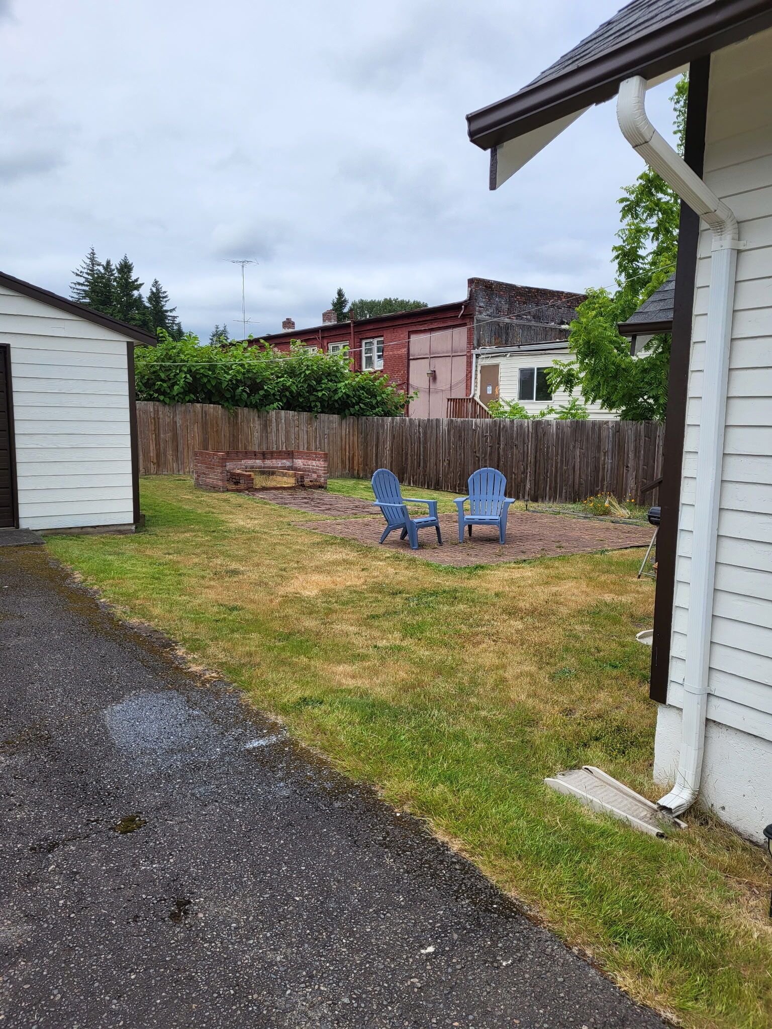 A backyard with two blue chairs, a brick fire pit, and a wooden fence.