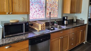 Una cocina con armarios de madera, microondas, cafetera y lavavajillas.