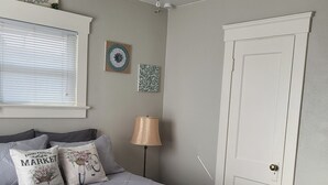 Un dormitorio con cama, ventilador de techo, ventana con persianas, puerta y adornos en la pared.