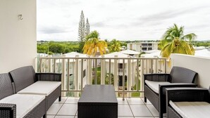 Ein Balkon mit Korbmöbeln, Blick auf Palmen und ein Gebäude im Hintergrund.