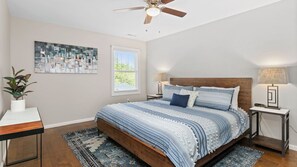 A bedroom with a large bed, two bedside tables with lamps, a ceiling fan, a window with blinds, and a wall-mounted abstract painting. - Cypress Sycamore by Avantstay 6 Mins to Downtown (Asheville)