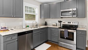 A modern kitchen with grey cabinets, stainless steel appliances, and a granite countertop. - Cypress Sycamore by Avantstay 6 Mins to Downtown (Asheville)