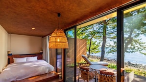 A bedroom with a large bed, a wooden ceiling, and a view of the beach through a glass door. - ISHINOYA Beppu (Beppu)