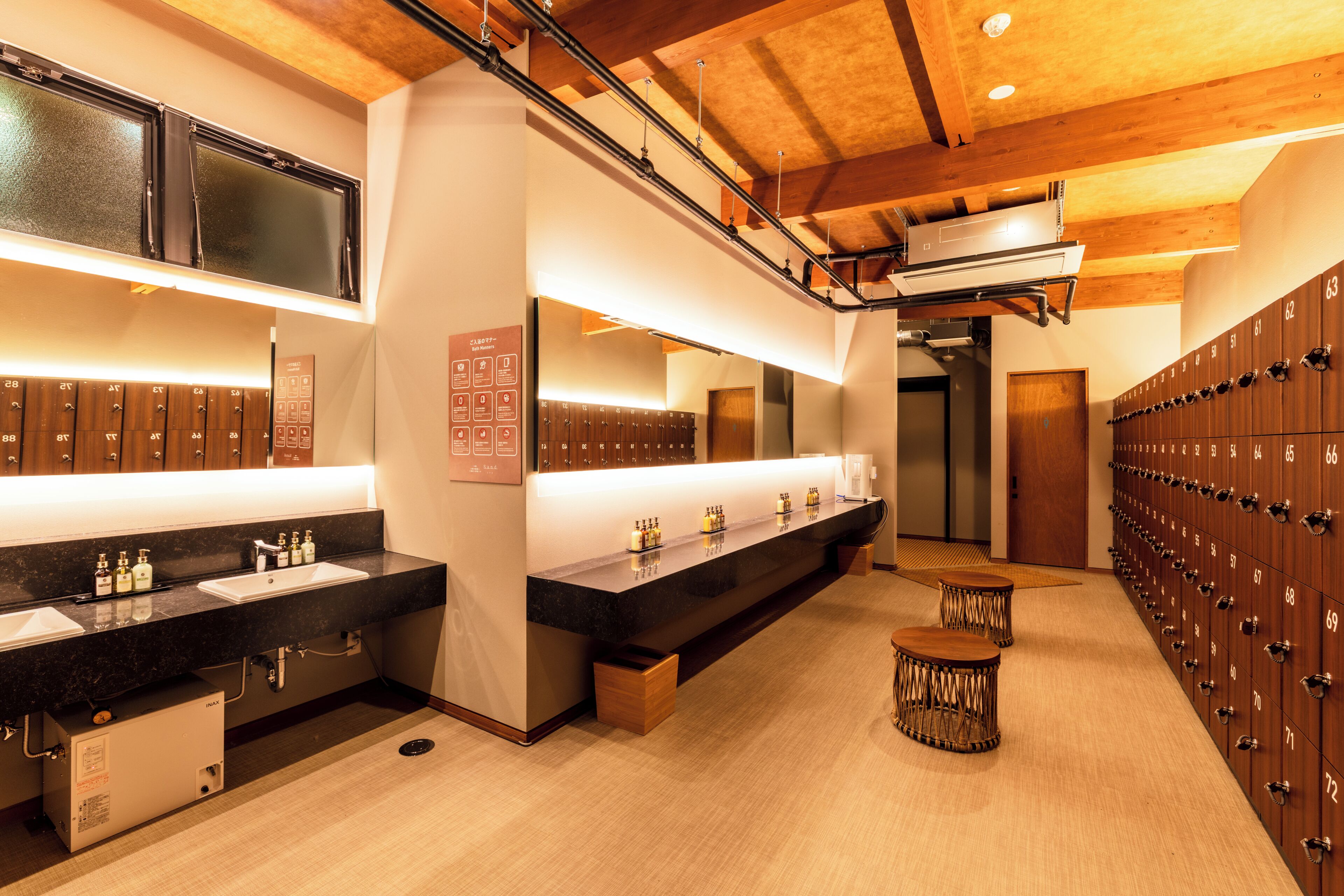 A modern bathroom with dual sinks, a large mirror, and a row of lockers.