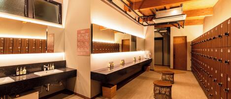 A modern bathroom with dual sinks, a large mirror, and a row of lockers.