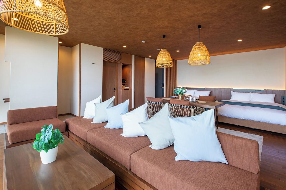A modern hotel room with a sofa, a dining table, and a bed.