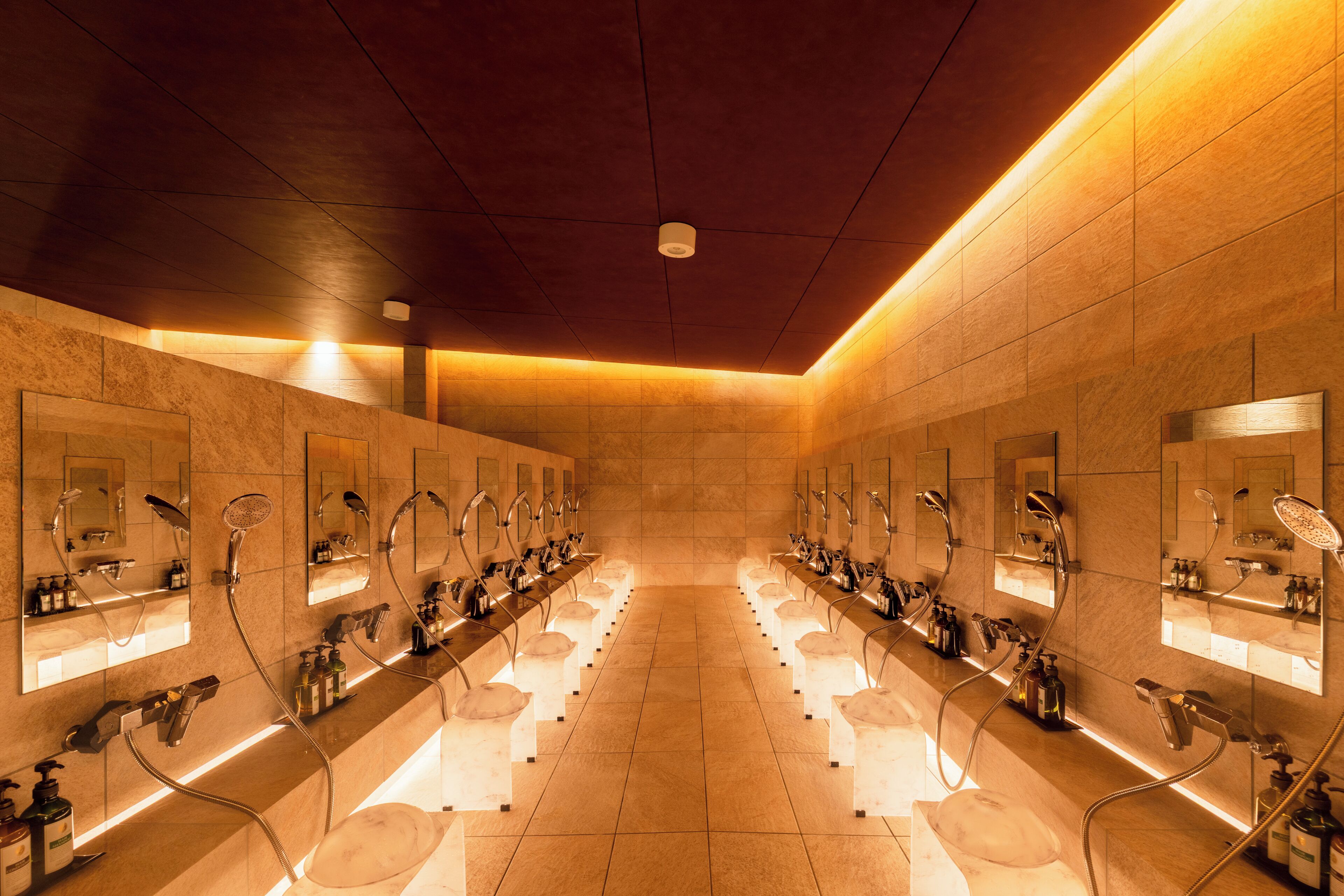 A row of individual wash stations with mirrors, sinks, and toiletries.