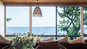 A dining area with a view of the sea, a wicker pendant light, and a table with a vase of flowers. - ISHINOYA Beppu (Beppu)
