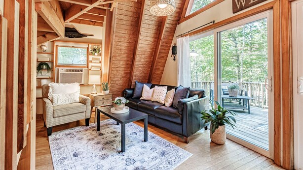 Ein gemütliches Interieur mit einem dunkelgrünen Ledersofa, einem Holzstuhl, einem Couchtisch und einem großen Fenster mit einem 'WELCOME'-Schild.