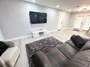 Ein modernes Wohnzimmer mit einem flachbildfernseher an der Wand, einer weißen Unterhaltungseinheit, einem grauen Sofa und einem gemusterten Teppich.