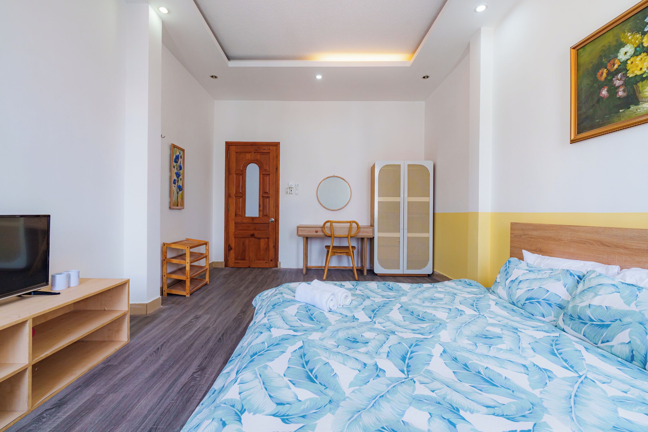 Hotellihuone, jossa on sänky, työpöytä, televisio, vaatekaappi ja taulu seinällä.