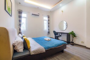 Habitación de hotel con cama, escritorio, silla, planta en maceta y ventana con cortinas.