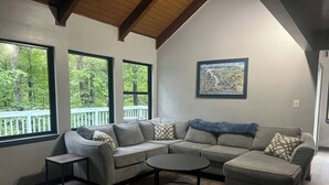 A modern living room with a sectional sofa, a small coffee table, and a view of a balcony with trees.