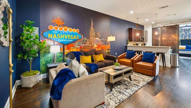 Una sala moderna con un mural de paisaje urbano, sofás de cuero y una pequeña zona de cocina.