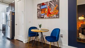 Una cocina moderna con electrodomésticos de acero inoxidable, una zona de comedor con sillas azules y una mesa redonda, y una pared decorada con un cartel de estilo vintage.