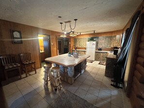 A kitchen with a central island, wooden chairs, a refrigerator, and a clock on the wall.