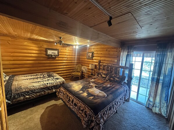 A log cabin bedroom with a large bed, a smaller bed, a chair, and a window with curtains.