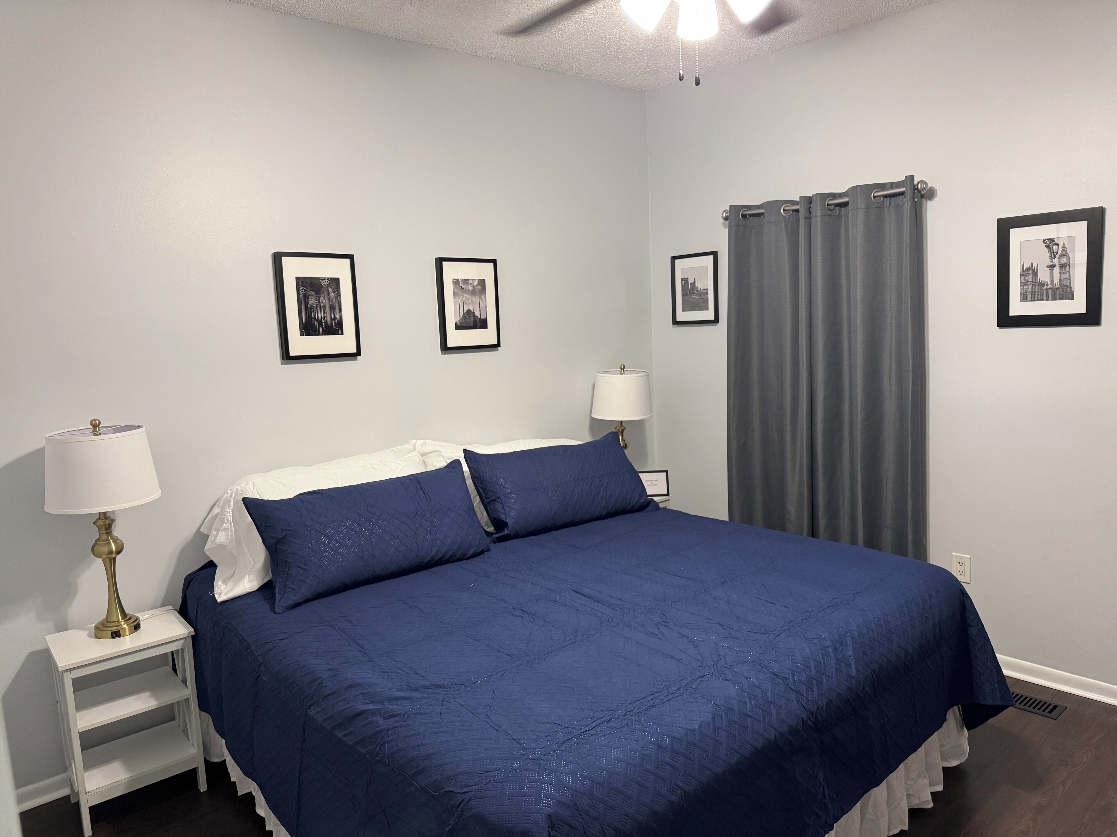 Une chambre à coucher avec un grand lit, deux tables de chevet avec des lampes et trois tableaux encadrés accrochés au mur.