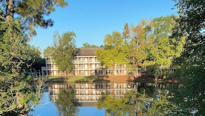 Un lago con el reflejo de un edificio, rodeado de árboles y un área cubierta de césped.