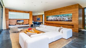 A spacious living area with a large white sectional sofa, a coffee table, and a TV mounted on a wooden wall. - At Last You and Your Friends Can Rent a Luxury Villa with 24/7 Concierge (Chang Wat Phang-nga)