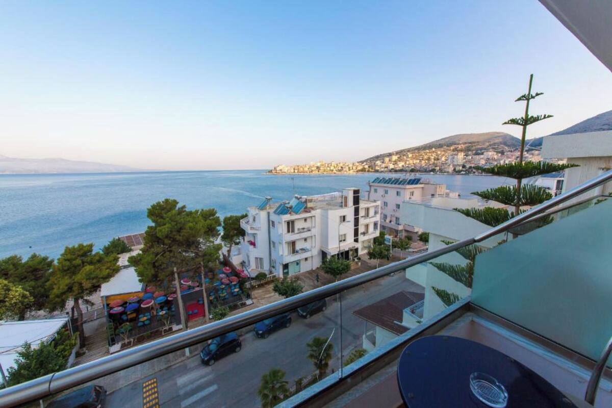 A balcony with a view of the sea, a restaurant with colorful umbrellas, and a building with solar panels.