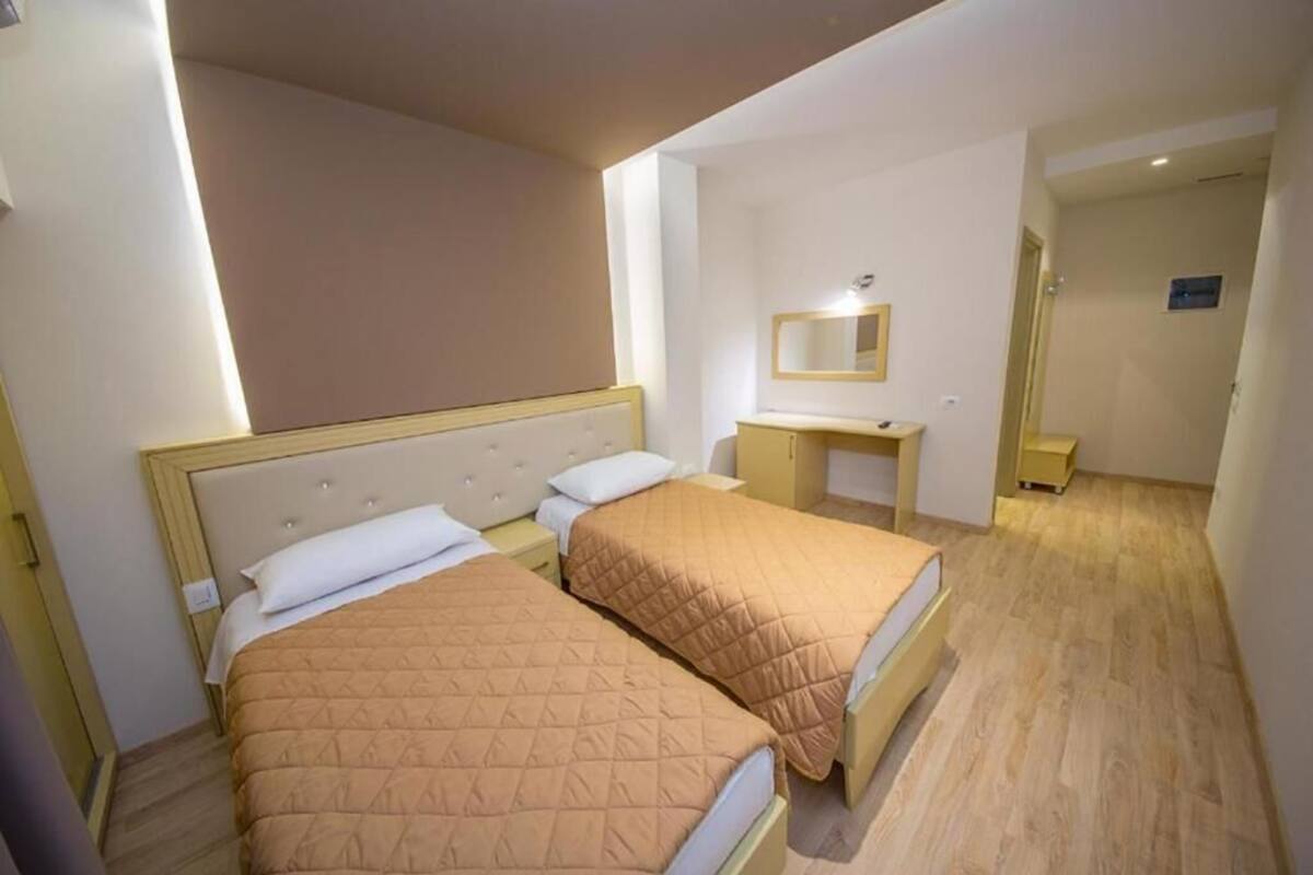 A hotel room with two beds, a desk, a mirror, and a small bathroom.