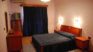Une chambre à coucher avec un lit double, deux tables de chevet, une commode, un téléviseur posé sur un meuble et une fenêtre avec des rideaux.