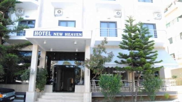 Un hôtel appelé « Hotel New Heaven », doté d’une façade moderne, d’une entrée abritée et d’un petit espace extérieur aménagé avec des sièges.