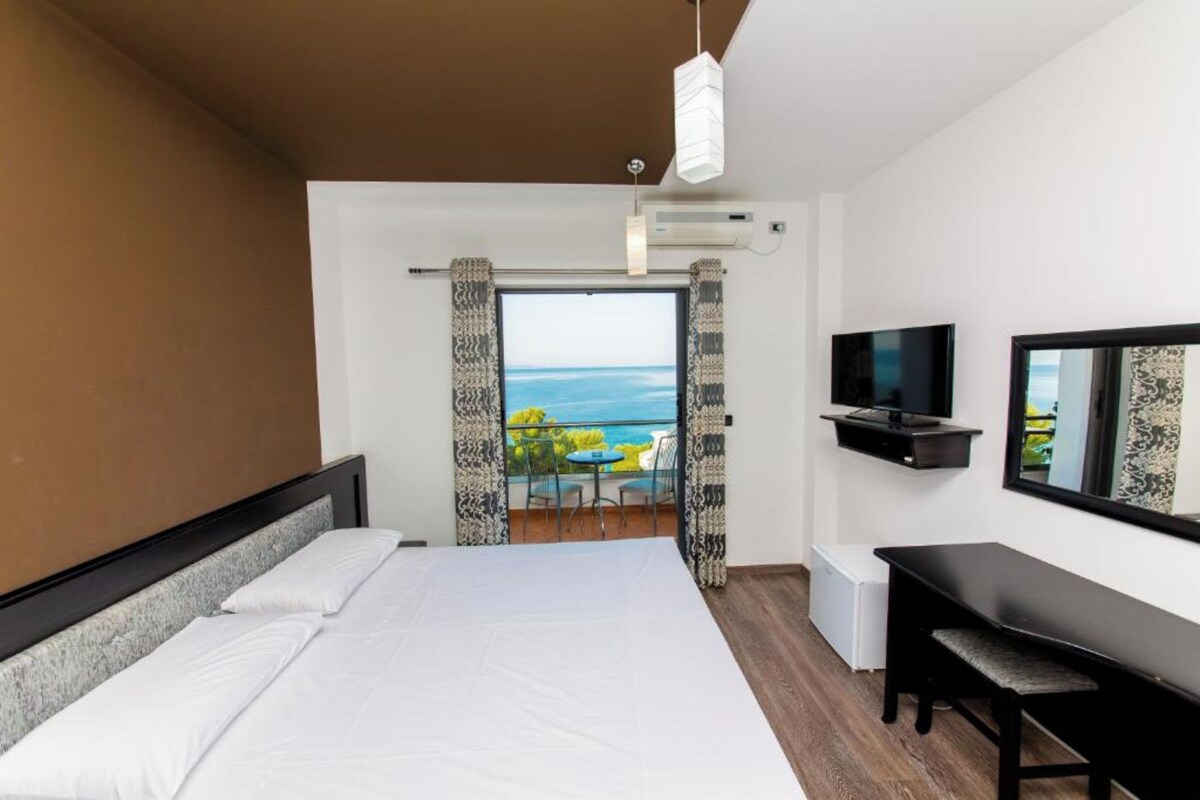 Una camera d'hotel con un letto, una scrivania, una televisione e un balcone vista mare.