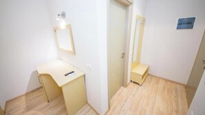 Une petite pièce propre, avec un plancher en bois, un bureau avec une chaise, un miroir et une porte.