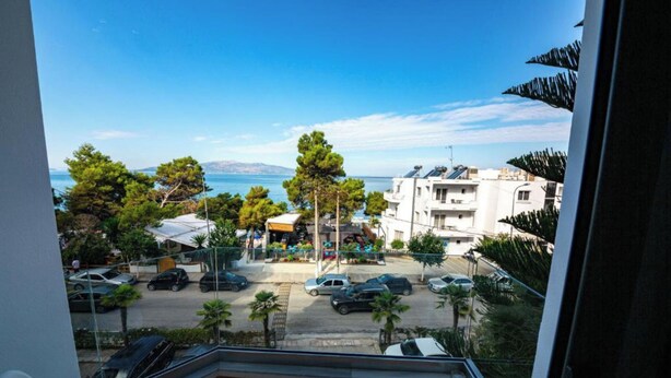 A balcony with a view of a parking area, buildings, and a clear sky. - New Heaven (Sarandë)