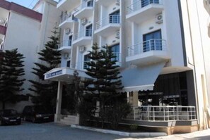 A multi-story hotel with balconies, a covered entrance, and a parking area. - New Heaven (Sarandë)