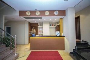Ein Hotel-Empfangsbereich mit Empfangstresen, mehreren Uhren, einer Treppe und einem roten Teppich.