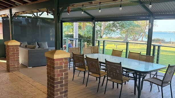 En overdækket terrasse med et bord og stole, murstenssøjler og udsigt til naturen.