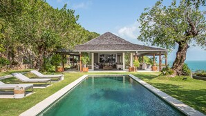 Una casa junto a la piscina con un patio cubierto, sillas de descanso y vistas al mar.