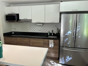 Una cocina moderna con armarios blancos, un refrigerador de acero inoxidable, un microondas y una encimera negra.