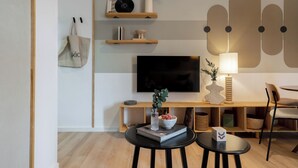 Una sala de estar moderna con una televisión de pantalla plana, estanterías de madera, una mesa de centro y un comedor con sillas.