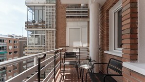 Un balcón con mesa y sillas, vista a edificios vecinos y un muro de ladrillo.
