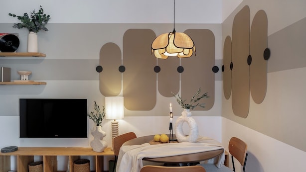 Una sala de estar moderna con televisor de pantalla plana, una mesa de comedor redonda y una lámpara colgante.