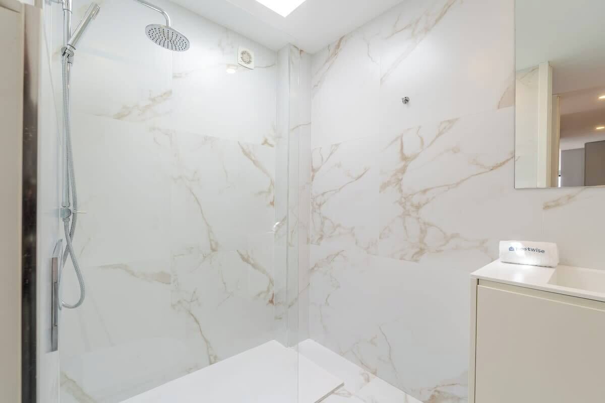 Une salle de bain moderne avec une douche à parois de verre, des murs en marbre et un meuble-lavabo blanc.