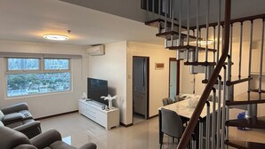 Una sala de estar moderna con televisor, sofá y comedor. Una escalera conduce a un nivel superior.