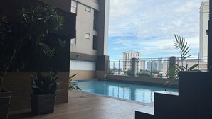 Un área de piscina en la azotea con vistas a edificios de la ciudad y un cielo despejado.