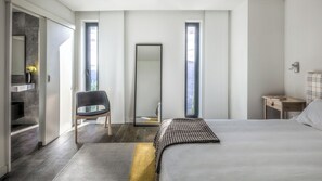 A modern bedroom with a large bed, a chair, a mirror, and a nightstand.