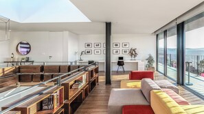 A modern living room with a large window, a sofa, a bookshelf, and a desk with a computer.