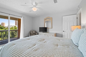 Ein Schlafzimmer mit einem Bett, einem Fernseher, einem Sessel, einer Tür und einem Balkon mit Blick auf Gebäude.