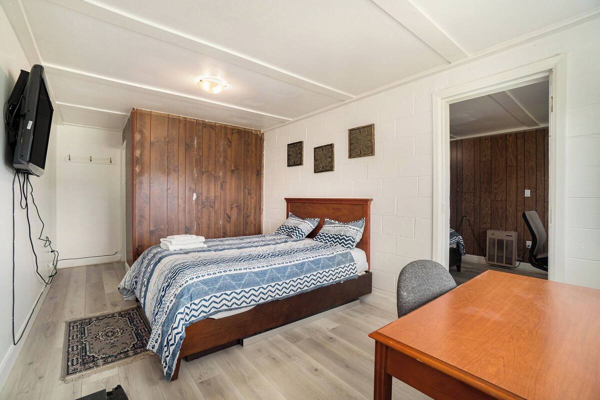 Une chambre avec un lit en bois, un téléviseur fixé au mur et une petite table.