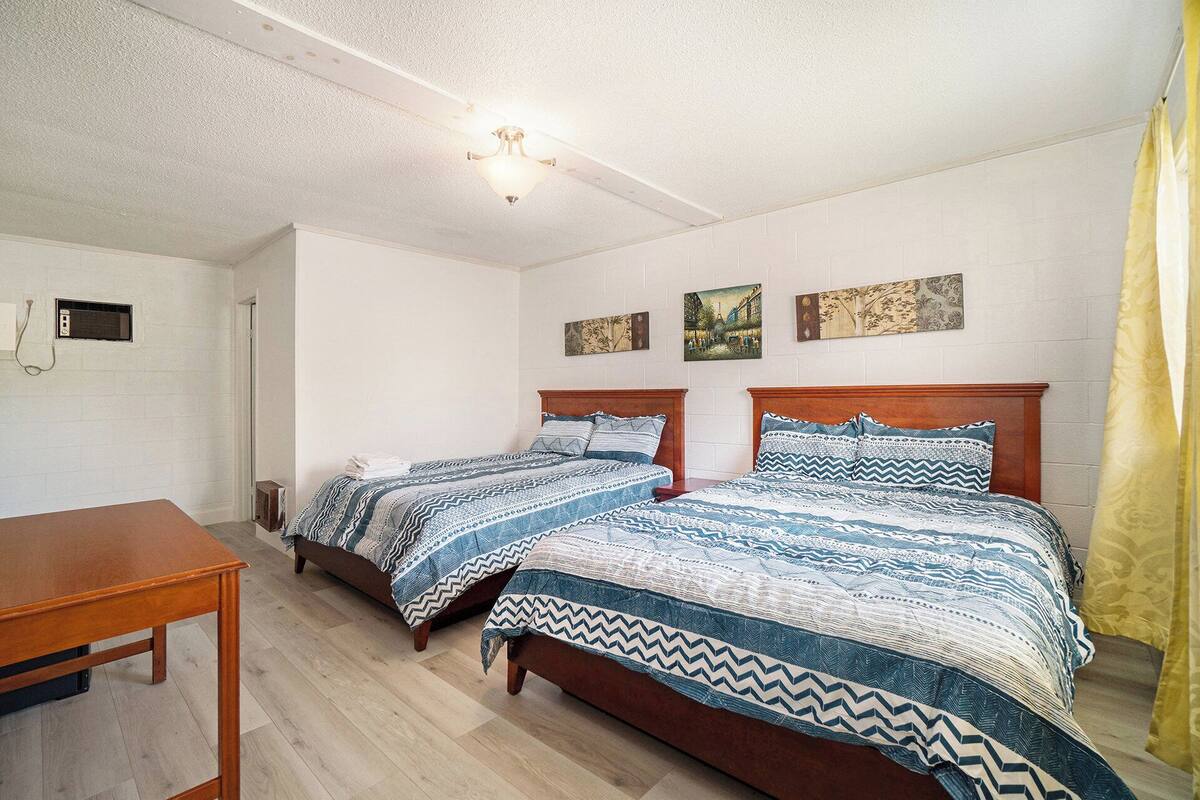 Une chambre avec deux lits, une table en bois et un luminaire fixé au plafond.
