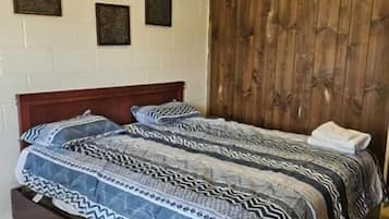 A bedroom with a wooden headboard, a patterned bedspread, and a white wall with three framed pictures.
