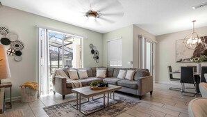 A modern living room with a sectional sofa, a coffee table, and a dining area with a chandelier. - Stylish 4BR Pool Townhome Storey Lake (Kissimmee)