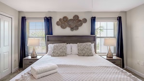 A bedroom with a large bed, two bedside tables with lamps, a decorative wall piece, and a window with curtains. - Stylish 4BR Pool Townhome Storey Lake (Kissimmee)